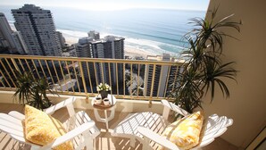 Een balkon met twee witte stoelen, een kleine tafel met een plant en uitzicht op het strand en de oceaan.