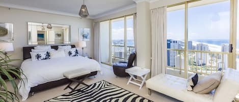 A spacious bedroom with a large bed, a sitting area, and a view of the city.
