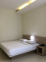 Una cama bien hecha con sábanas y almohadas blancas, una mesita de noche con lámpara y un teléfono a la derecha.