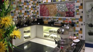 A modern kitchen with a colorful tile backsplash, a fruit-themed wall art, and a water dispenser. - Msquare Hotel (Palembang)