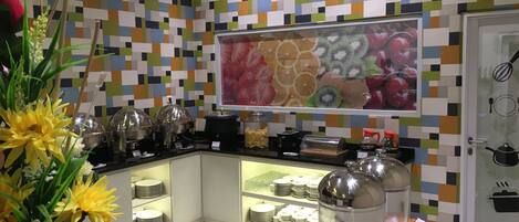 A modern kitchen with a colorful tile backsplash, a fruit-themed wall art, and a water dispenser.