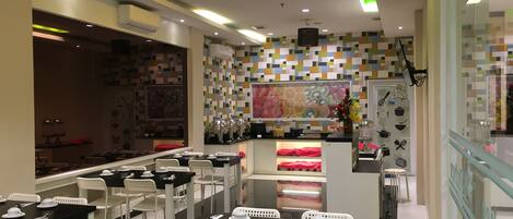 A restaurant with white chairs and black tables, a colorful mosaic wall, and a teal pendant light.