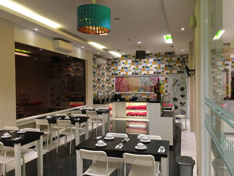 A restaurant with white chairs and black tables, a colorful mosaic wall, and a teal pendant light.