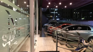A hotel entrance with a glass facade, a metal staircase, and a row of parked cars outside. - Msquare Hotel (Palembang)