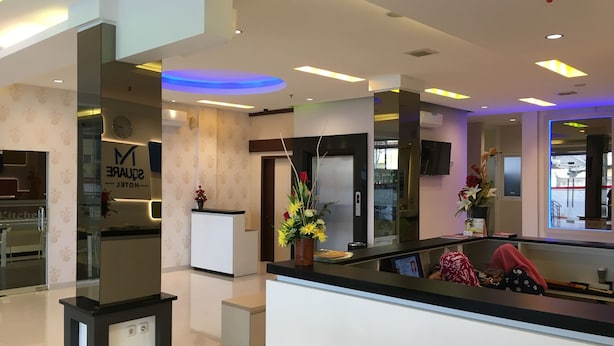 A hotel reception area with a modern design, including a reception desk, a clock, and a floral arrangement. - Msquare Hotel (Palembang)