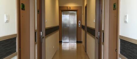 A hotel corridor with wooden doors, a central elevator, and a tiled floor.