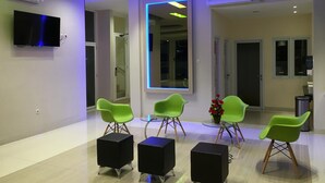 A modern waiting area with green chairs, black ottomans, and a flat-screen TV on the wall. - Msquare Hotel (Palembang)