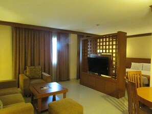 A hotel room with a sofa, a coffee table, a TV, and a dining area with chairs. - Patra Jakarta (Jakarta)