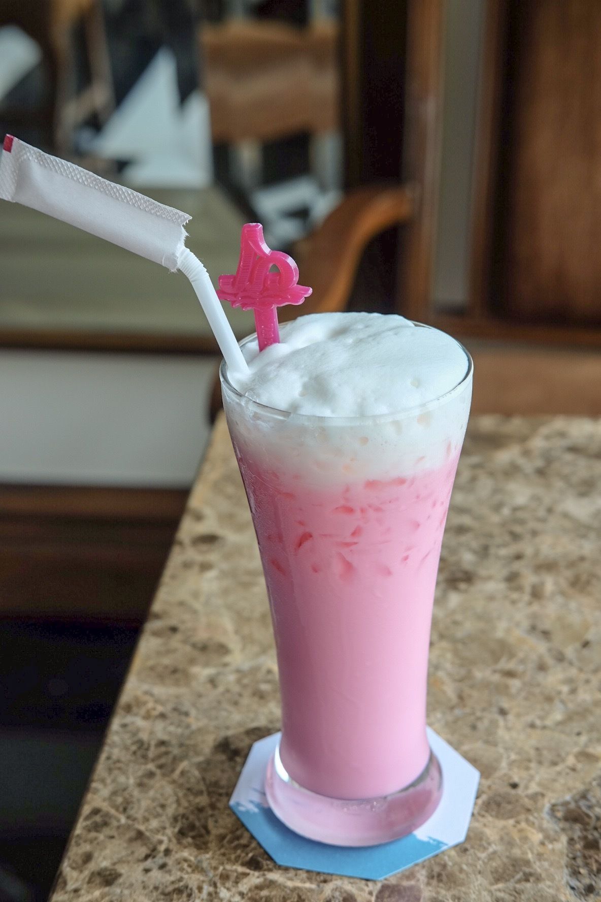 A pink beverage with a white straw and a pink straw topper on a coaster.