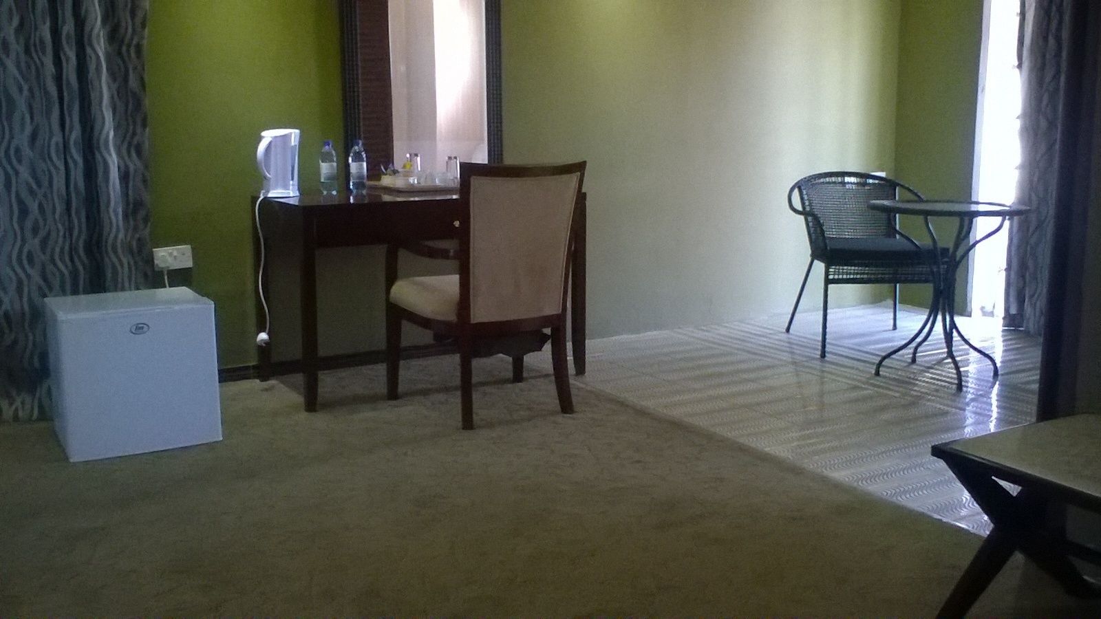 A room with a dining table, a chair, a small white appliance, and a chair by a window.