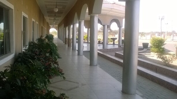 A covered corridor with columns, potted plants, and a tiled floor. - Sahara Stones Hotel (Palapye)
