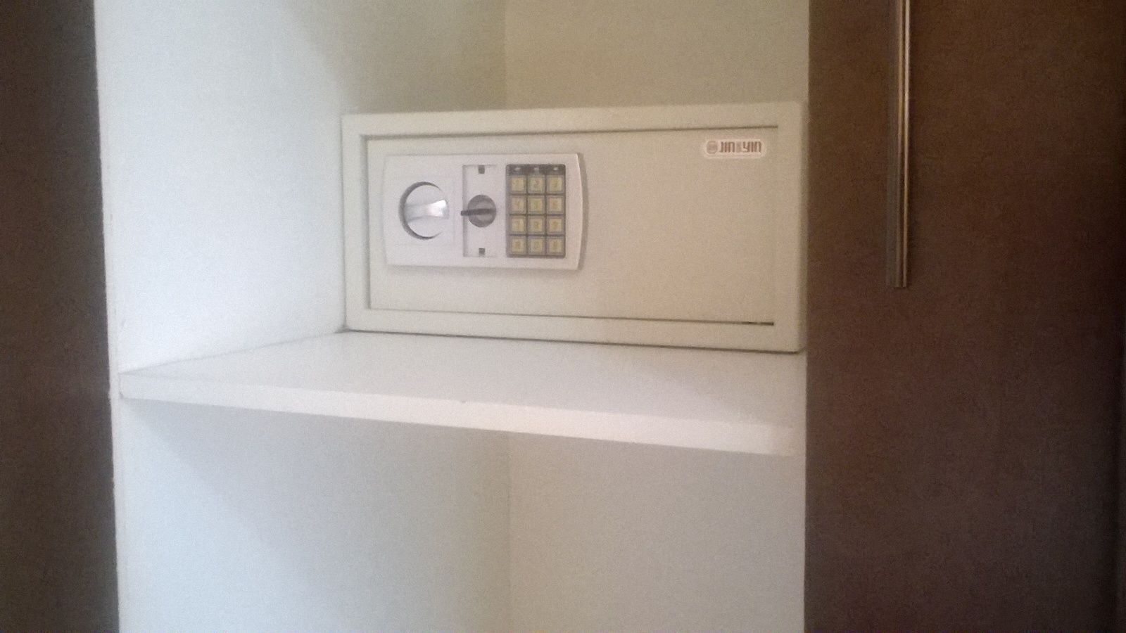 A white safe in a corner of a room with a brown door.