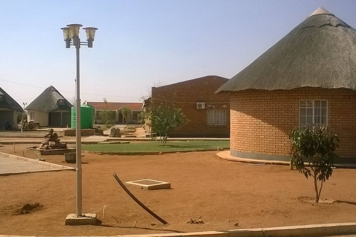 A rural setting with thatched-roof buildings, a paved area, and a street lamp.