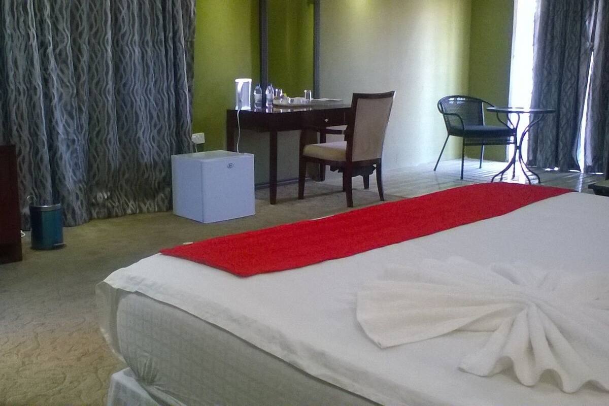 A hotel room with a bed, a desk, a chair, a TV, and a small white cabinet.