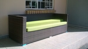 A wicker bench with a green cushion, positioned against a wall with a window above it. - Sahara Stones Hotel (Palapye)