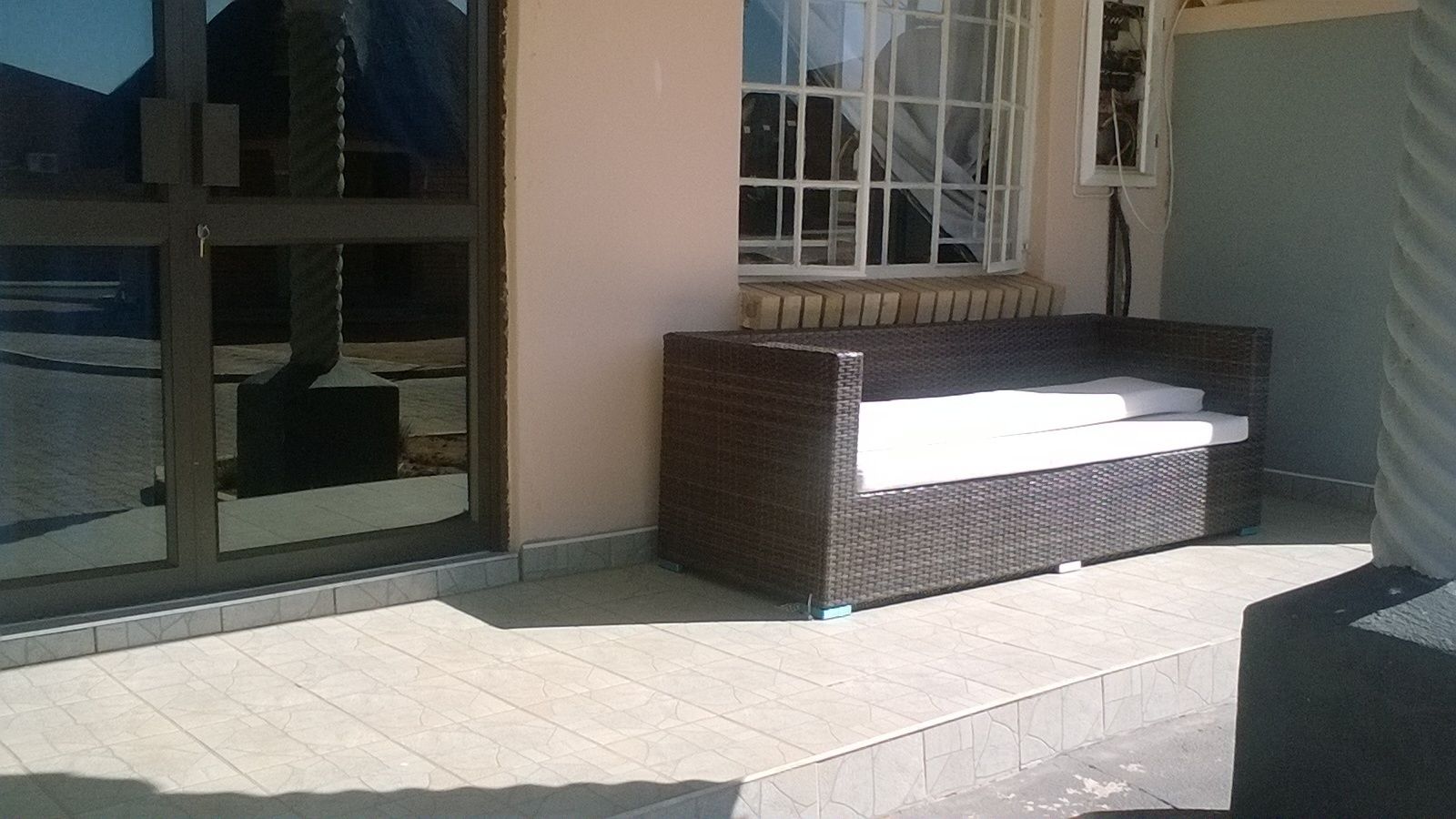 A wicker sofa with a white cushion against a wall, next to a glass door with a metal frame.