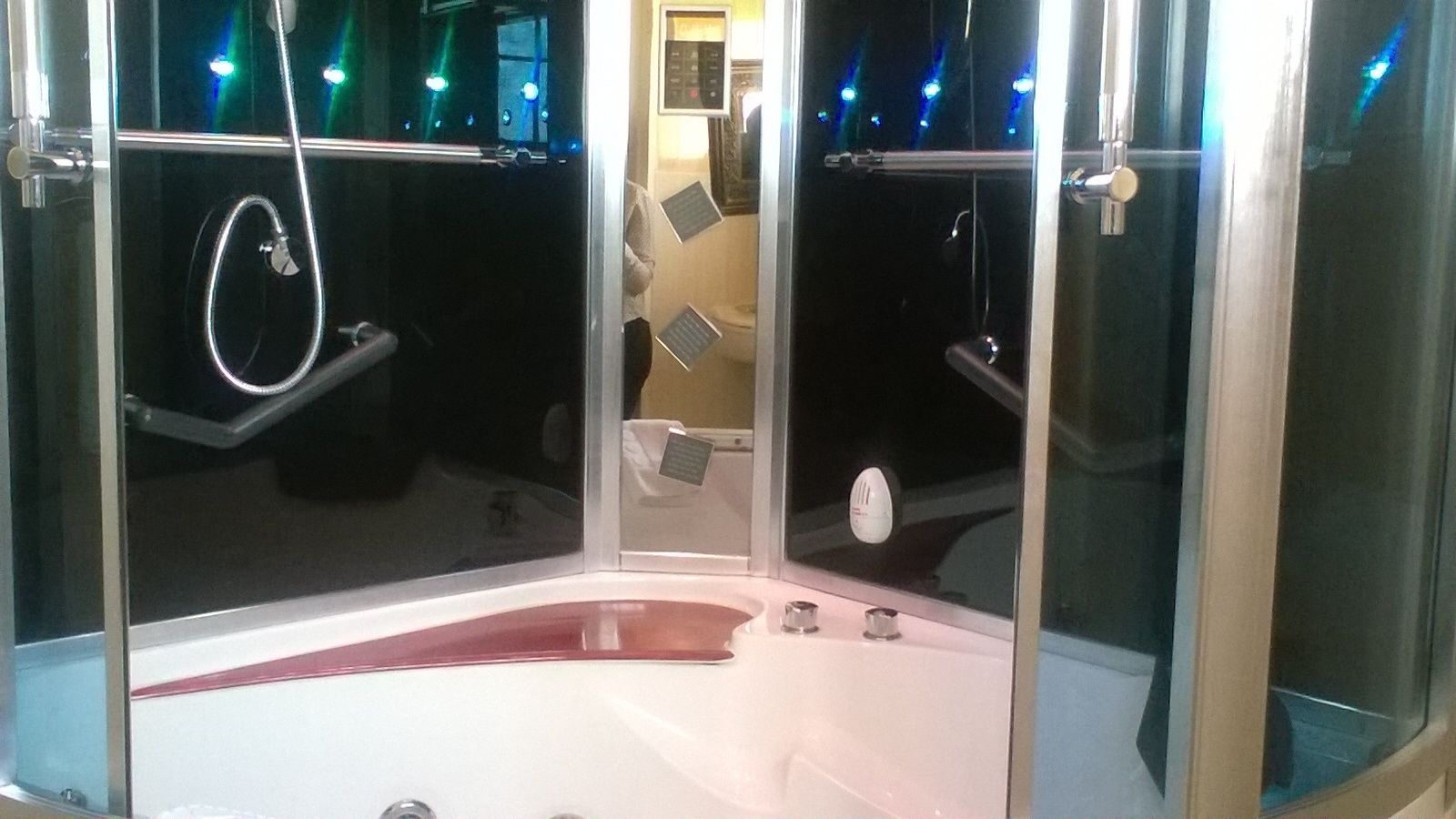 A modern bathroom with a glass-enclosed shower, a white bathtub, and a visible control panel.