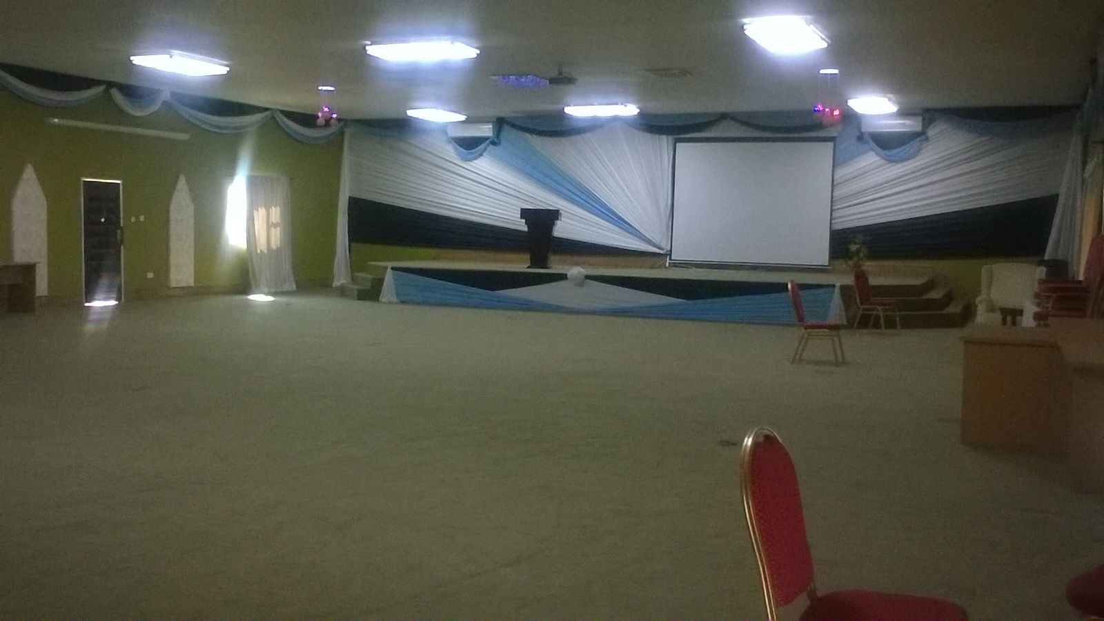A large hall with a stage, chairs, and a projector screen.