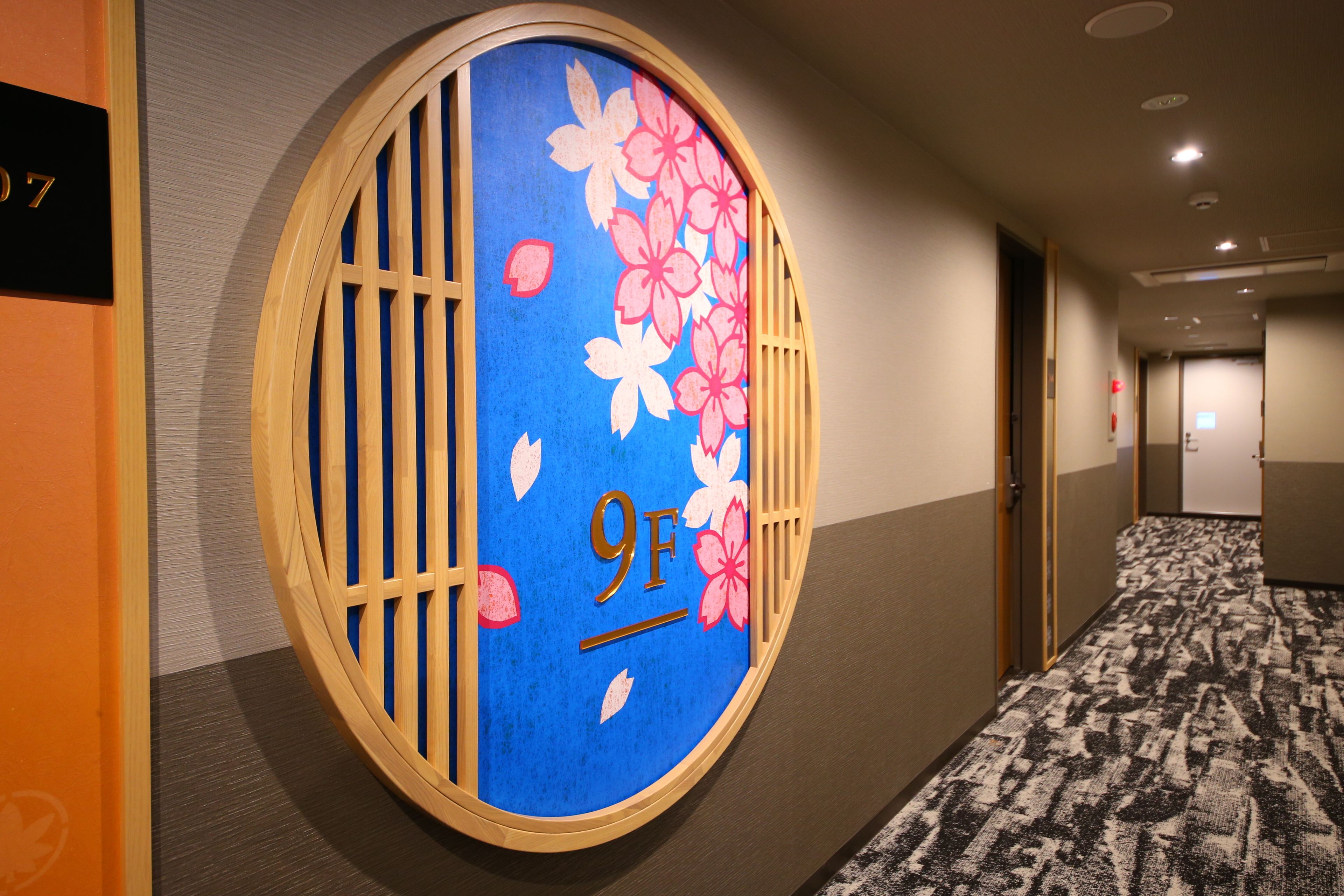 A hallway with a circular sign indicating room 9F, featuring a blue background with pink cherry blossoms.