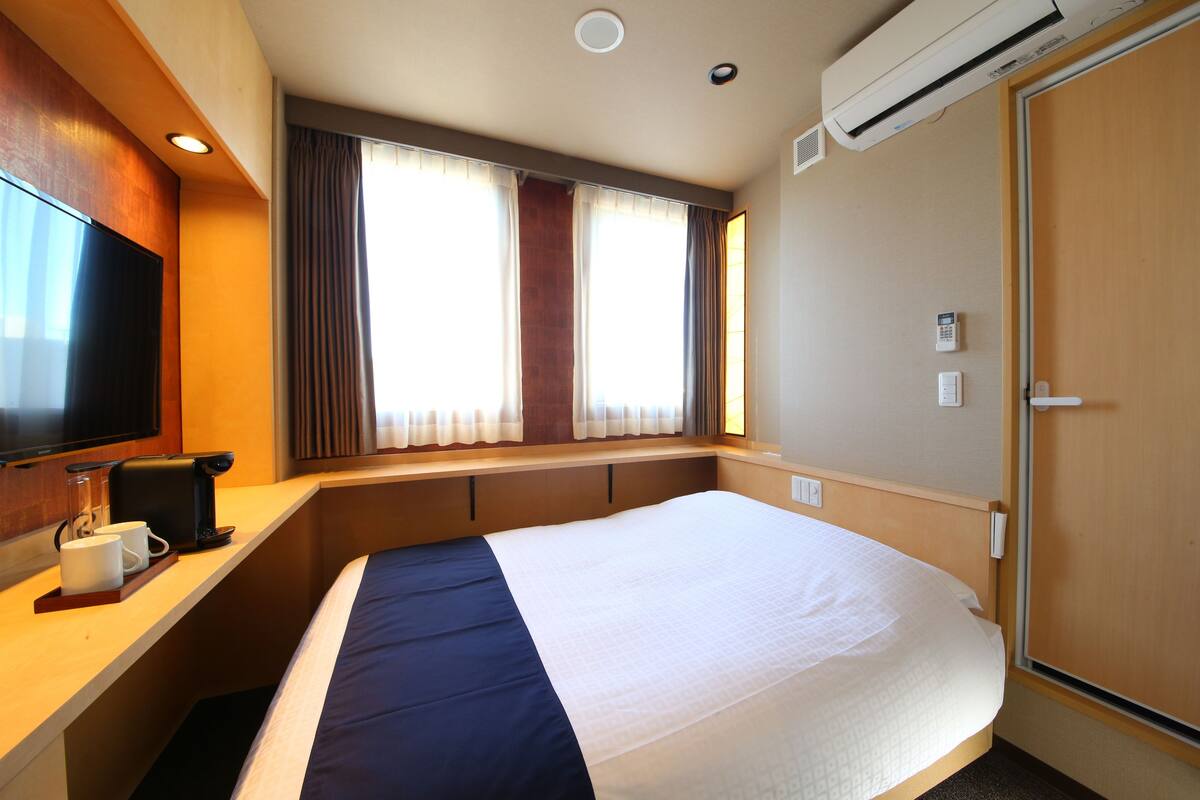 Een hotelkamer met een bed, een televisie, een bureau met koffiezetapparaat, en een raam met gordijnen.