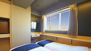 Een hotelkamer met twee bedden, een bureau, een stoel en een raam met gordijnen.