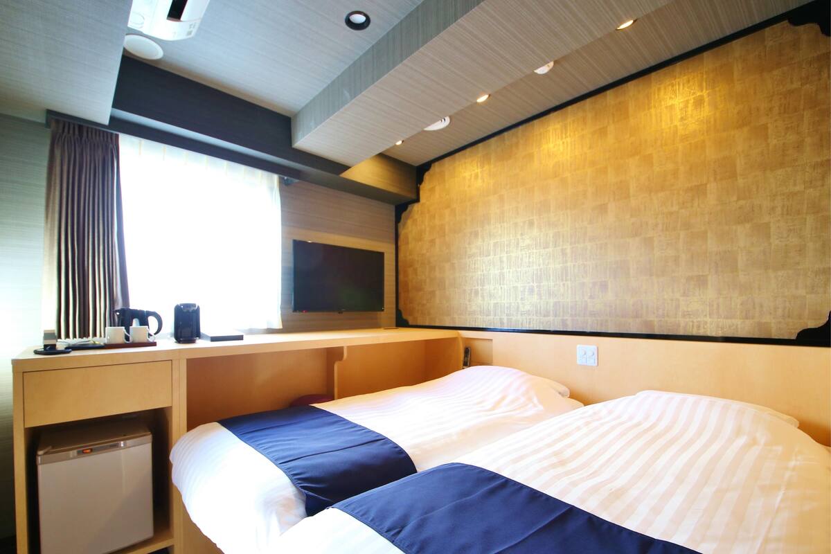Een hotelkamer met een bed, een bureau, een kleine koelkast, een raam met gordijnen en een televisie aan de muur.