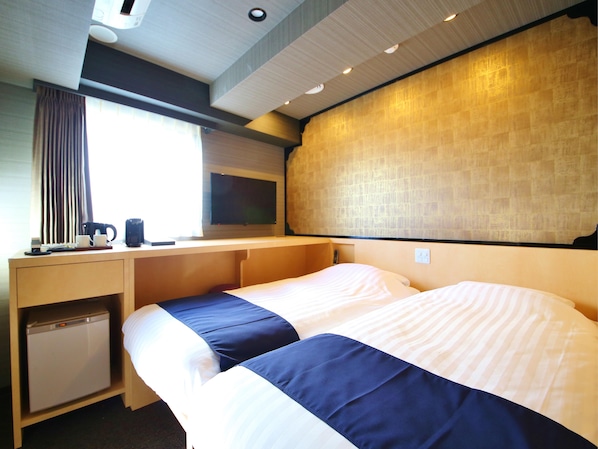 Een hotelkamer met een bed, een bureau, een kleine koelkast, een raam met gordijnen en een televisie aan de muur.