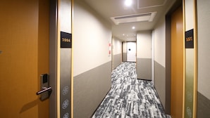 Un couloir d’hôtel avec des portes numérotées 1006 et 1001, un sol recouvert de moquette et un plafond doté d’un éclairage encastré.