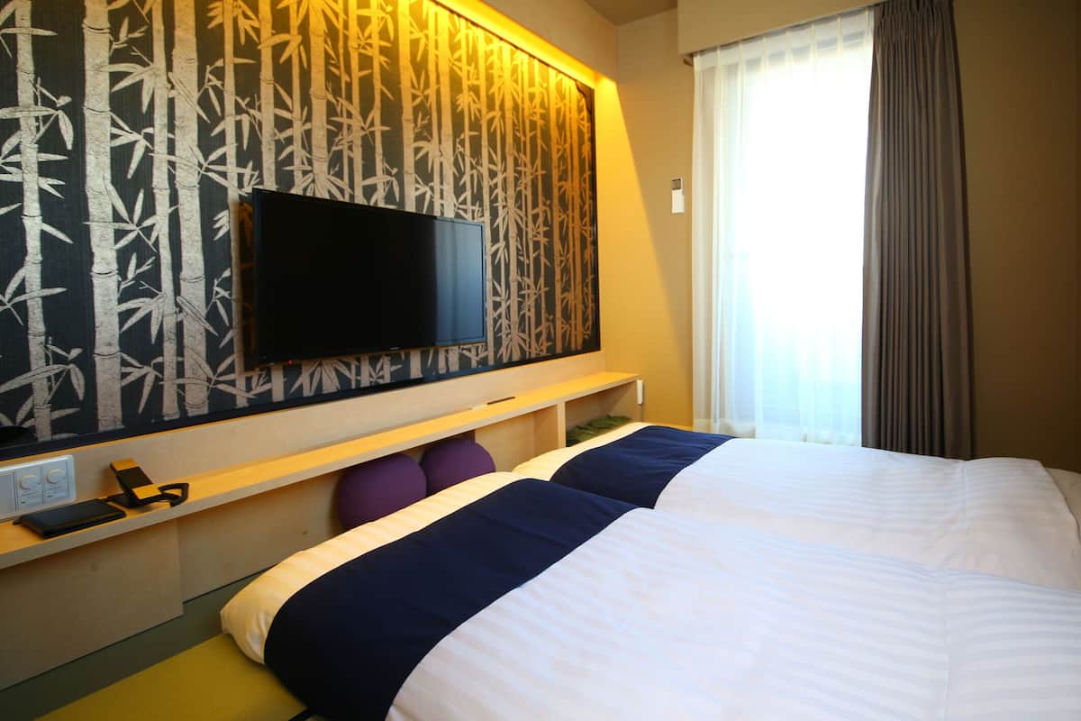 Een hotelkamer met een bed, een aan de muur bevestigde televisie, een raam met gordijnen en een muur met een bamboepatroon.