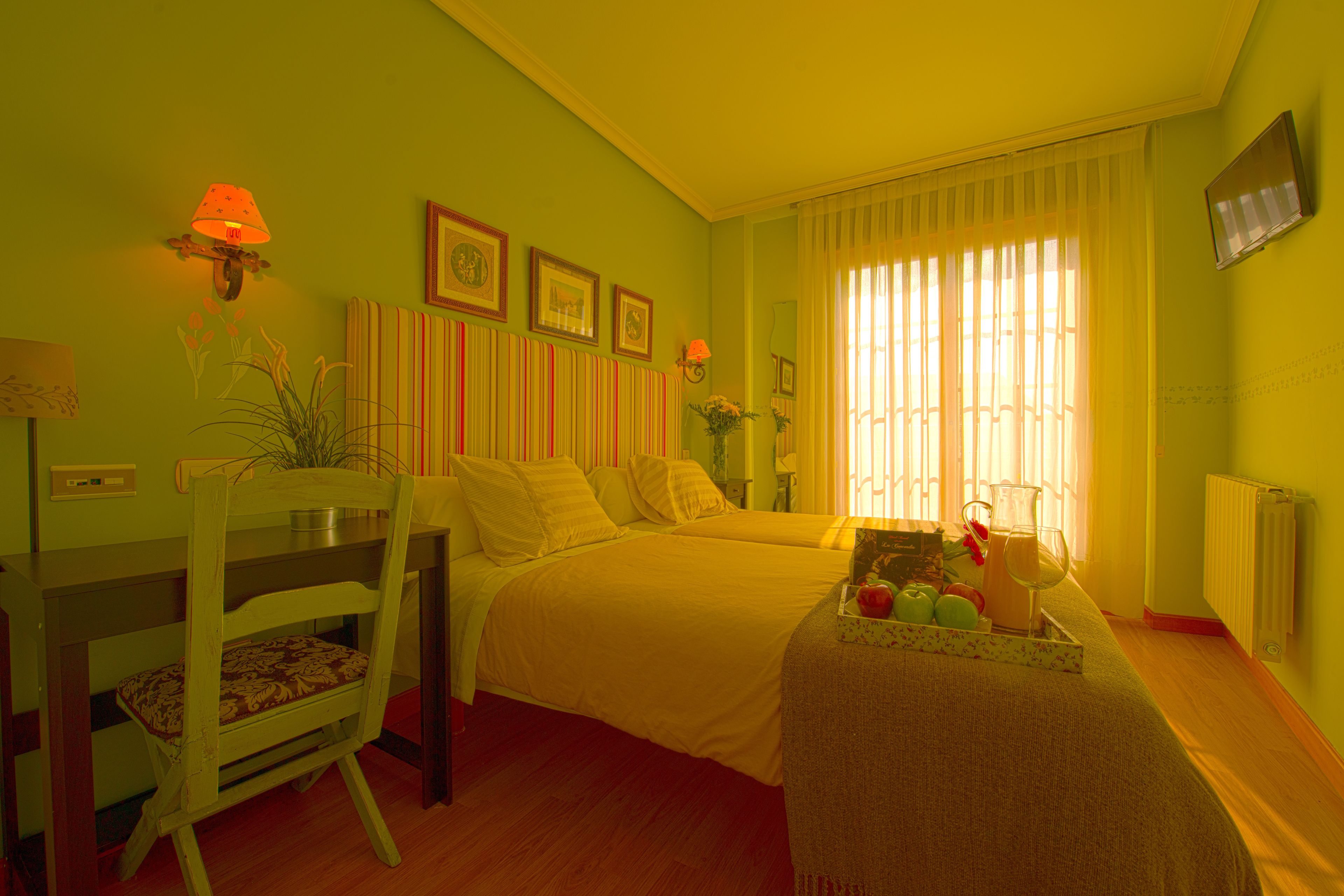 Habitación con dos camas, una mesa de comedor, sillas, una lámpara y una mesita con una jarrón y manzanas.