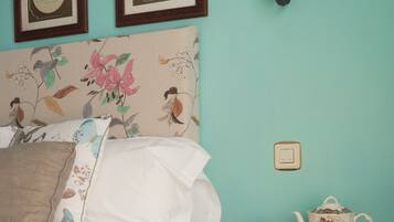 A bedroom with a bed, a nightstand with a teapot and cup, and two framed certificates on the wall.