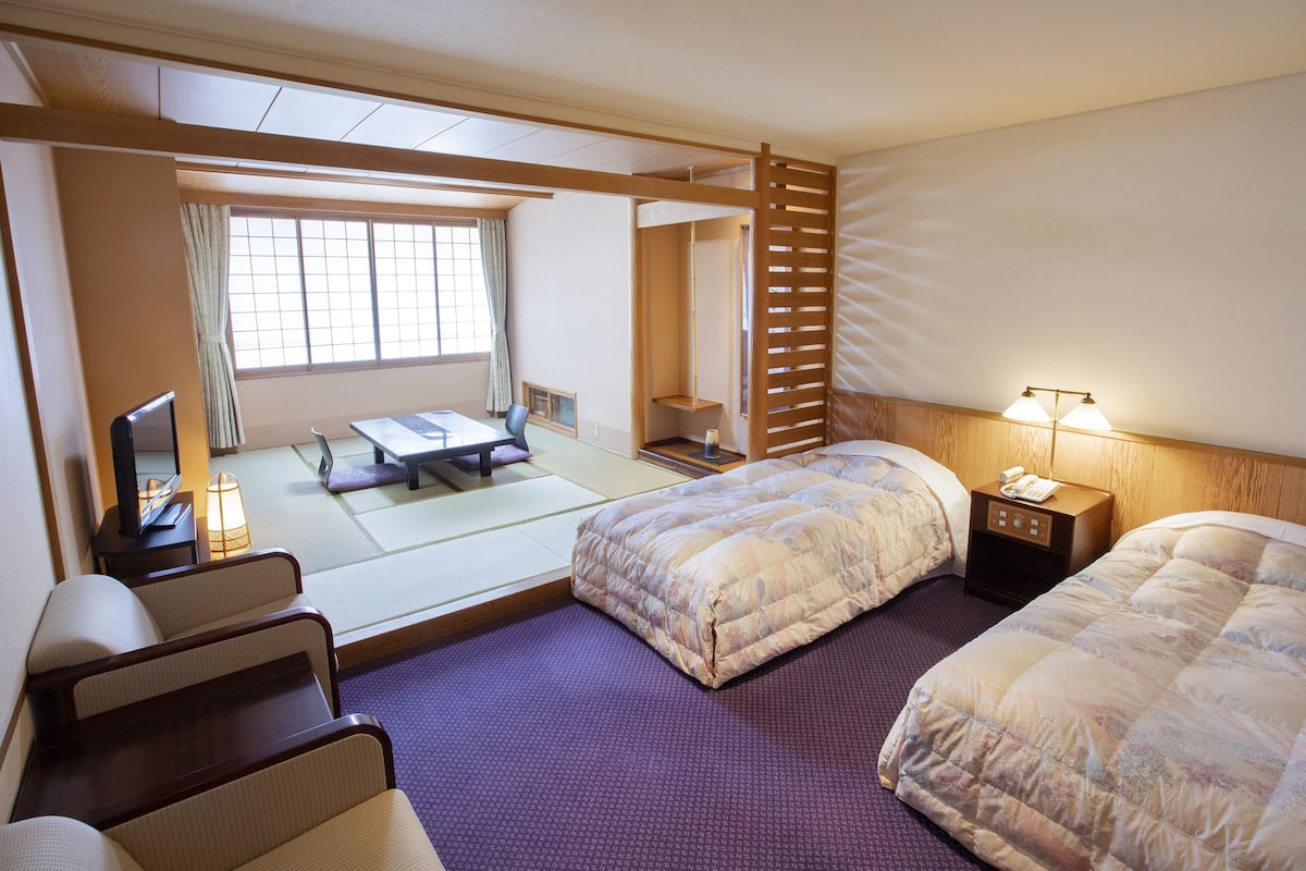 A traditional Japanese-style hotel room with tatami flooring, a futon bed, a separate sofa, and a sliding shoji screen.