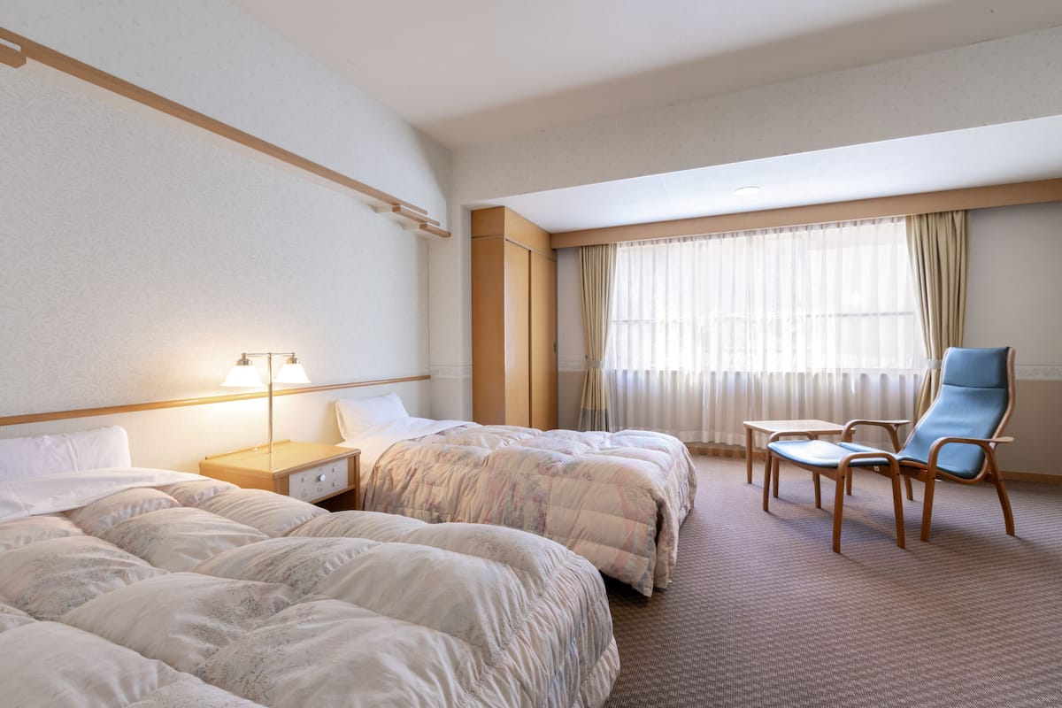 A hotel room with two beds, a desk, a chair, and a large window with curtains.