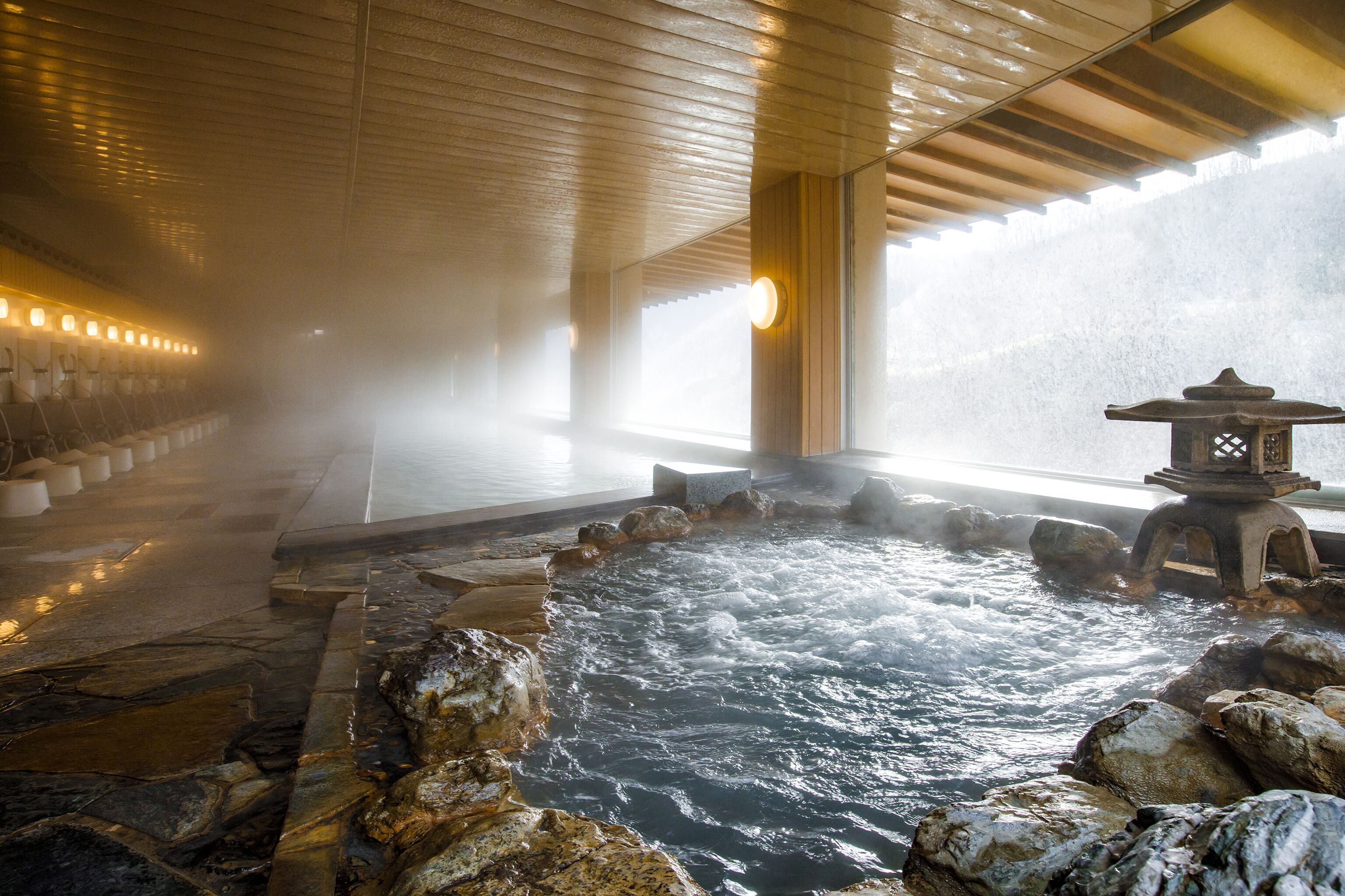 A hot spring area with stone flooring, a stone lantern, and a wooden ceiling.