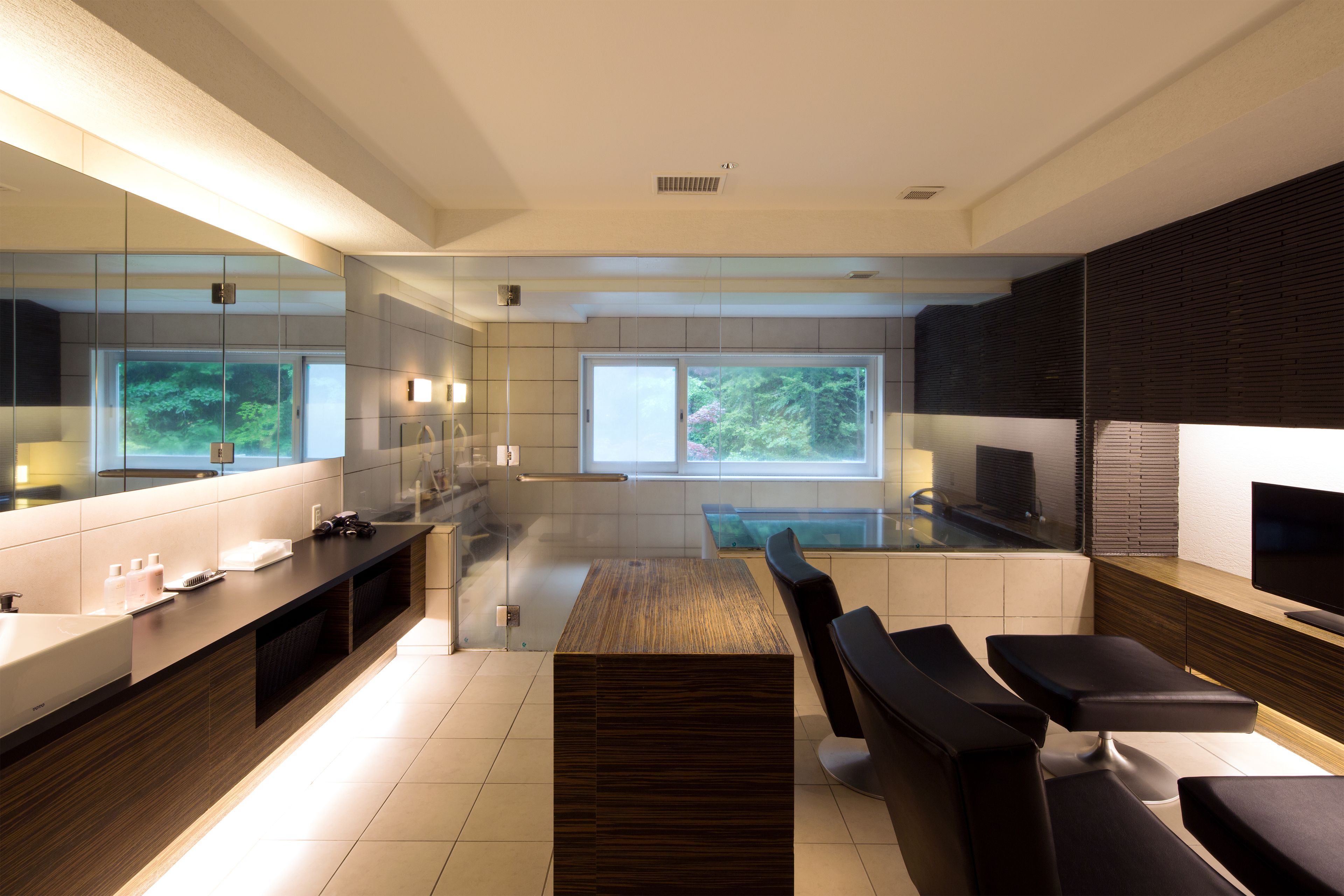 A modern kitchen with a large island, built-in appliances, and a large window providing a view of greenery outside.