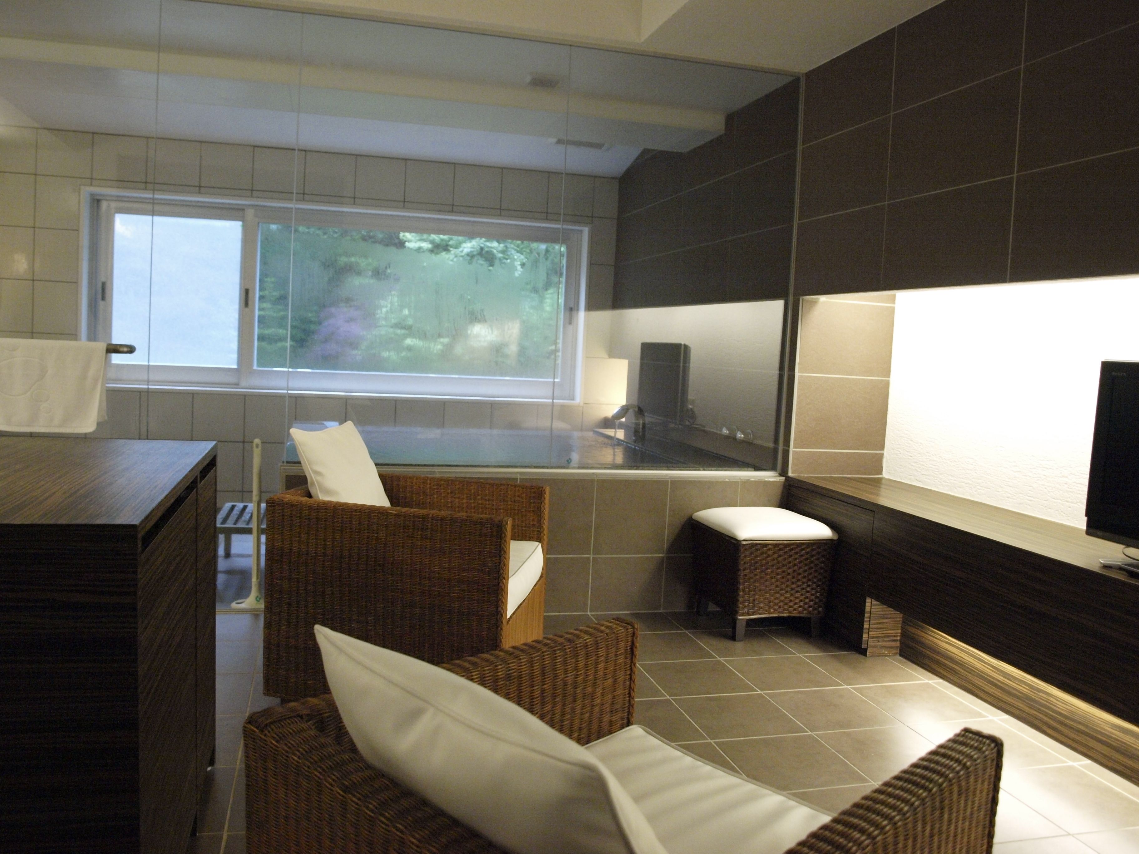 A modern bathroom with a bathtub, a large window, and wicker furniture.