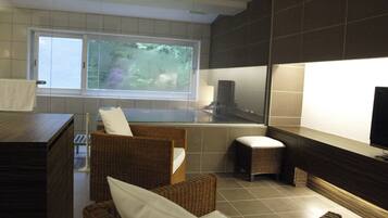 A modern bathroom with a bathtub, a large window, and wicker furniture.