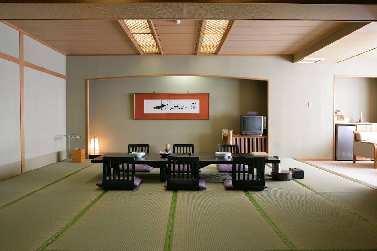 A traditional Japanese-style room with tatami flooring, a low table, and black chairs.