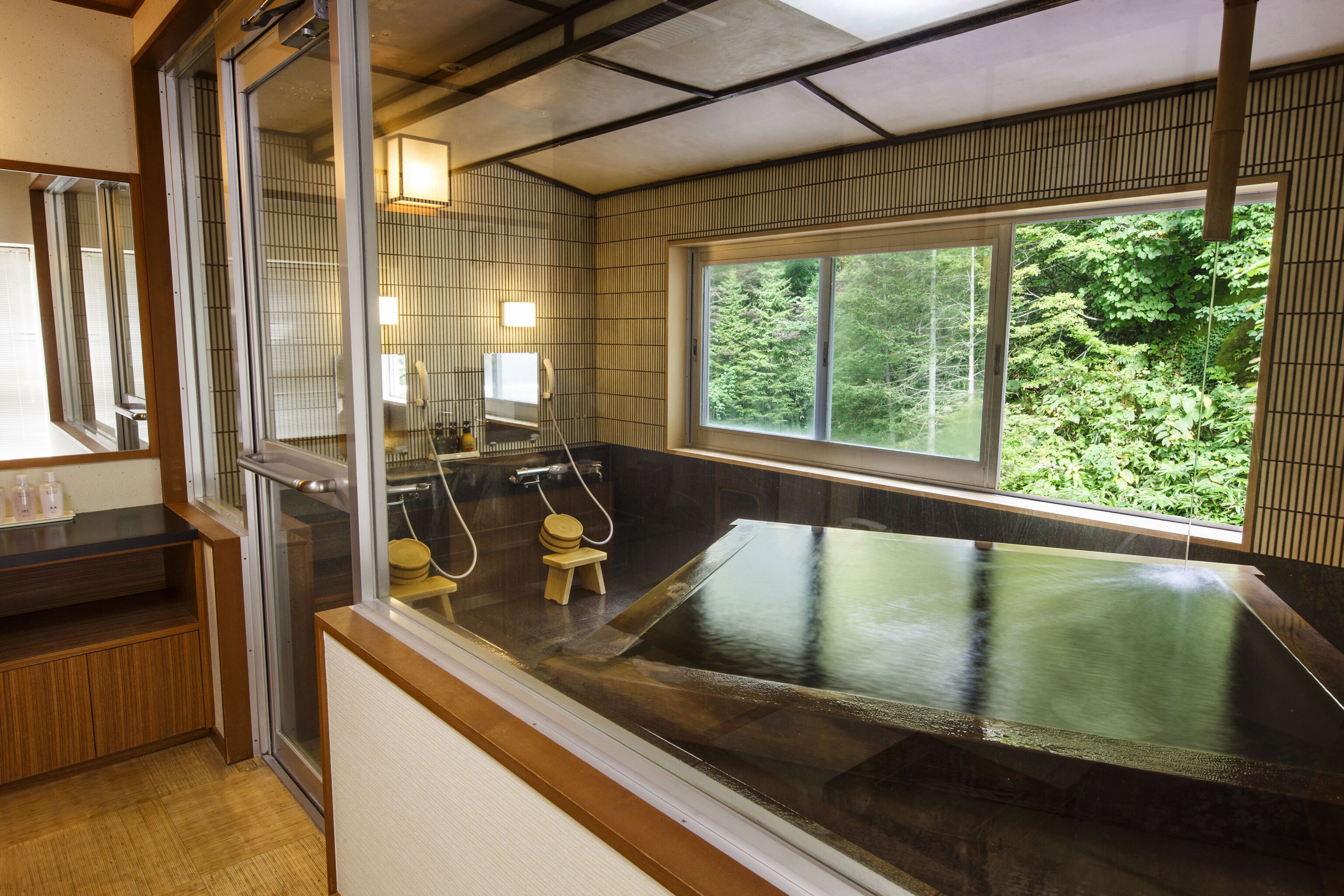 A traditional Japanese onsen with a wooden bench, a small wooden stool, and a glass enclosure.