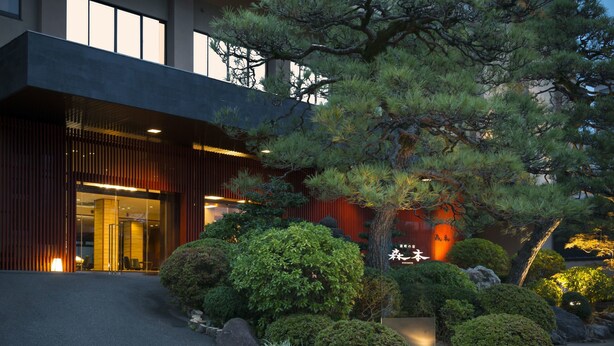 Un edificio moderno con entrada de vidrio, rodeado de arbustos cuidados y un árbol grande.