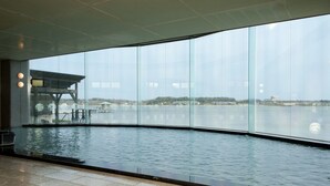 Una piscina interior moderna con amplios ventanales que ofrecen vistas a una masa de agua y edificios distantes.