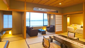 Una habitación de estilo japonés tradicional con suelo de tatami, una mesa baja, dos sofás y una cama con vistas al mar.