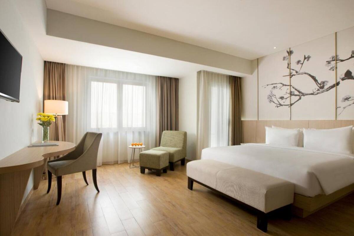 Une chambre d’hôtel avec un lit, un bureau, une chaise, une petite table avec des fruits et un téléviseur.