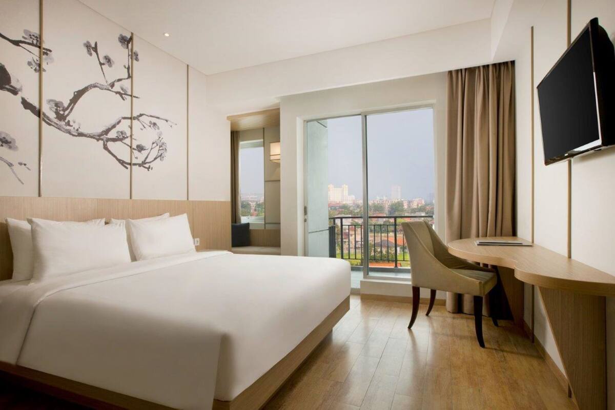 Une chambre d’hôtel avec un grand lit, un bureau, une chaise, une télévision et un balcon offrant une vue sur la ville.