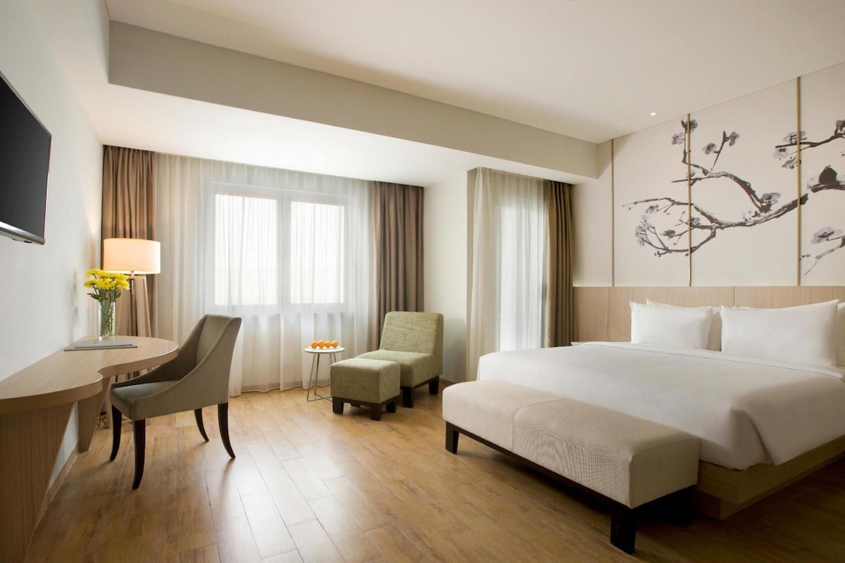 Ein Hotelzimmer mit einem Bett, einem Schreibtisch, einem Stuhl, einem Fernseher und einem Fenster mit Vorhängen.