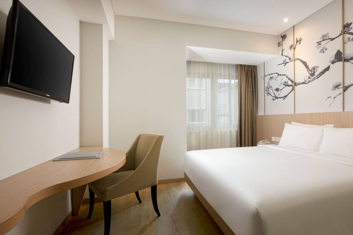 Une chambre d’hôtel équipée d’un lit, d’un bureau, d’une chaise, d’une télévision et d’une fenêtre avec des rideaux.