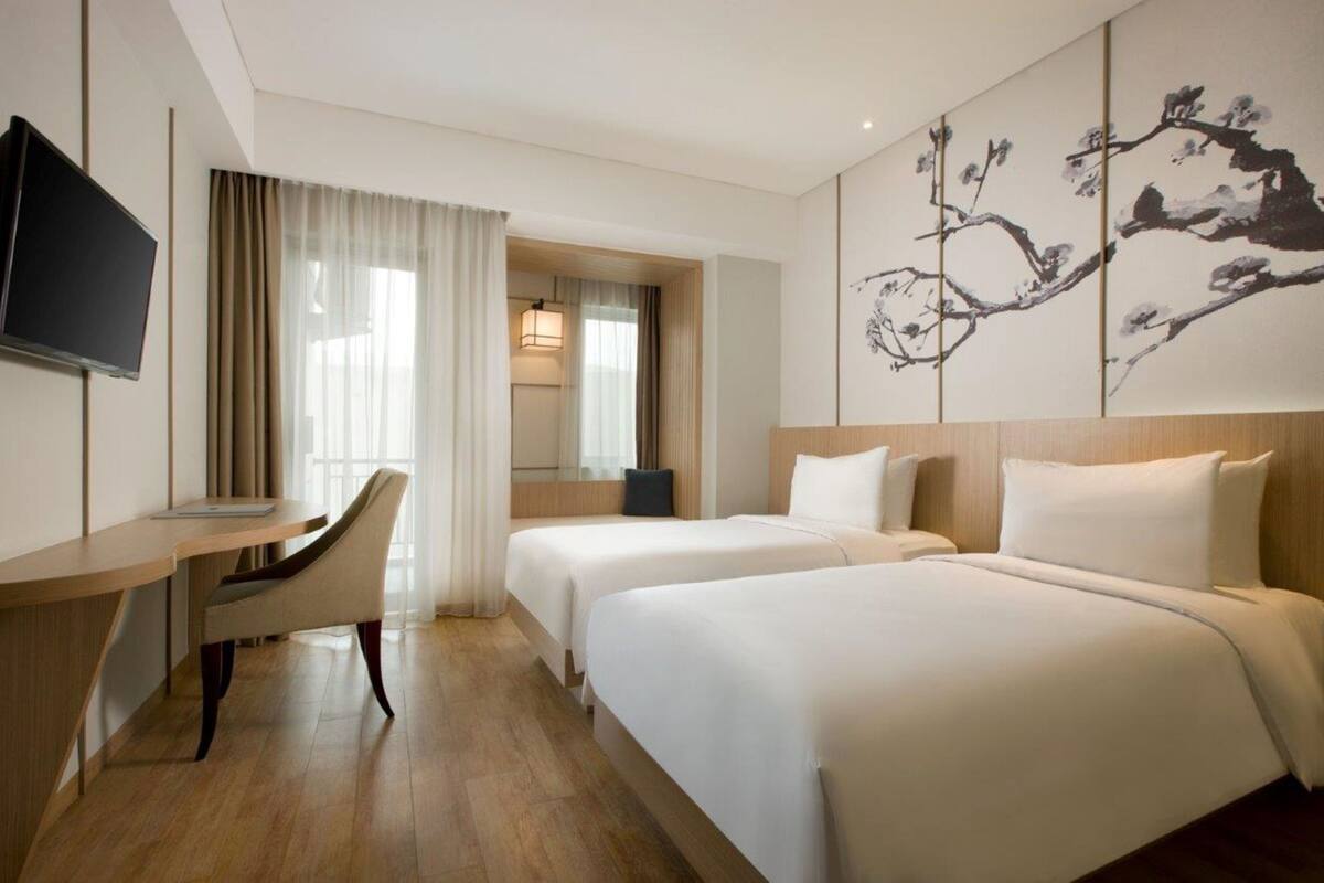 Une chambre d’hôtel avec deux lits, un bureau, une chaise, une télévision et un grand tableau au mur.