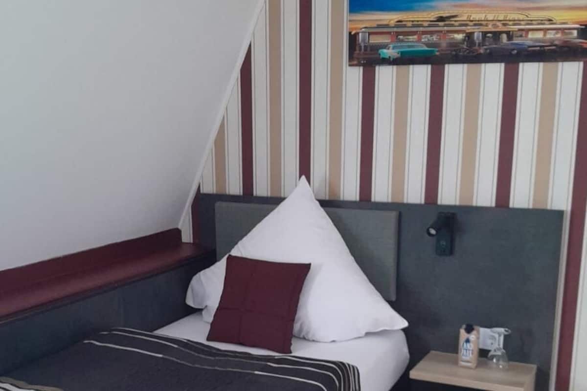 A hotel room with a bed, a nightstand, a painting, and striped wallpaper.