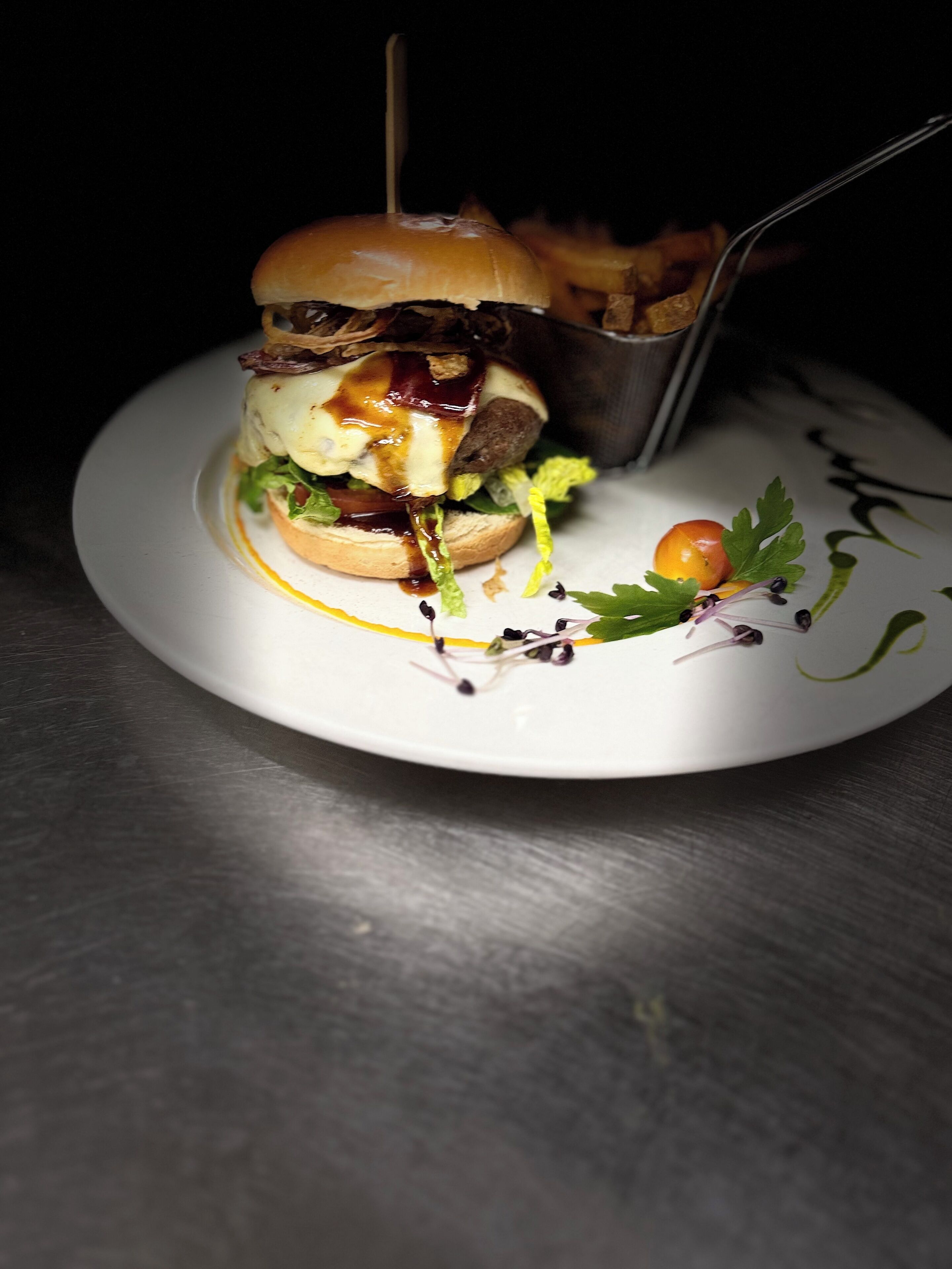 A burger with a toothpick on a white plate, garnished with greens and a cherry tomato.