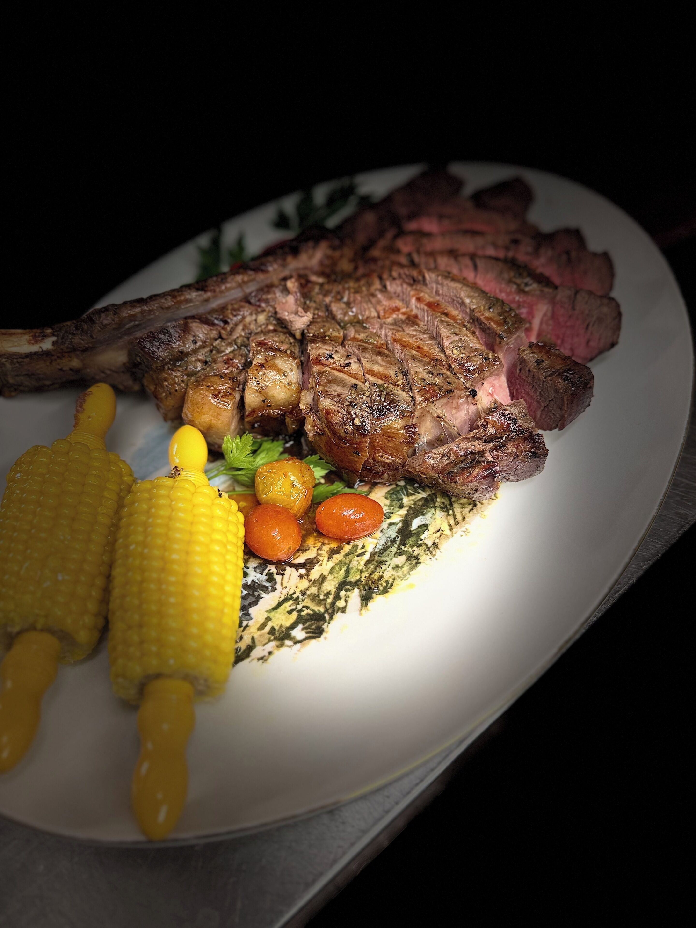 A plate with a grilled steak, corn on the cob, and cherry tomatoes.